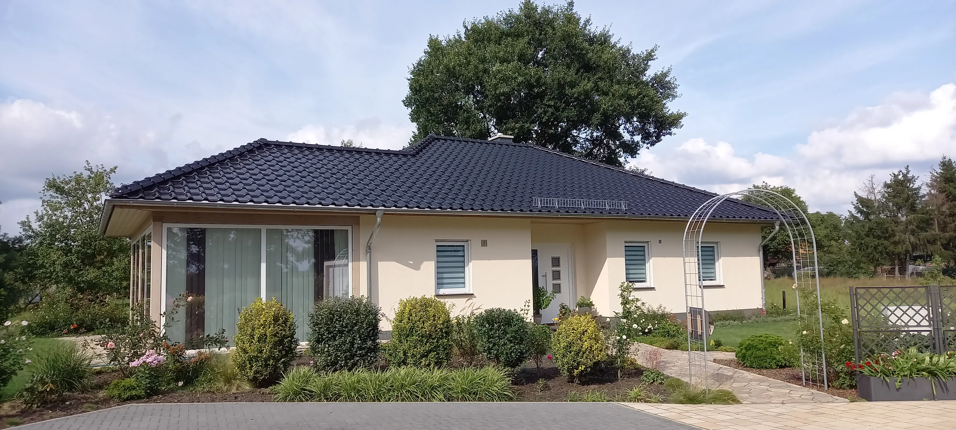 Moderner, ebenerdiger Bungalow mit dunklem Walmdach, großzügiger Fensterfront und gepflegter Gartenanlage.